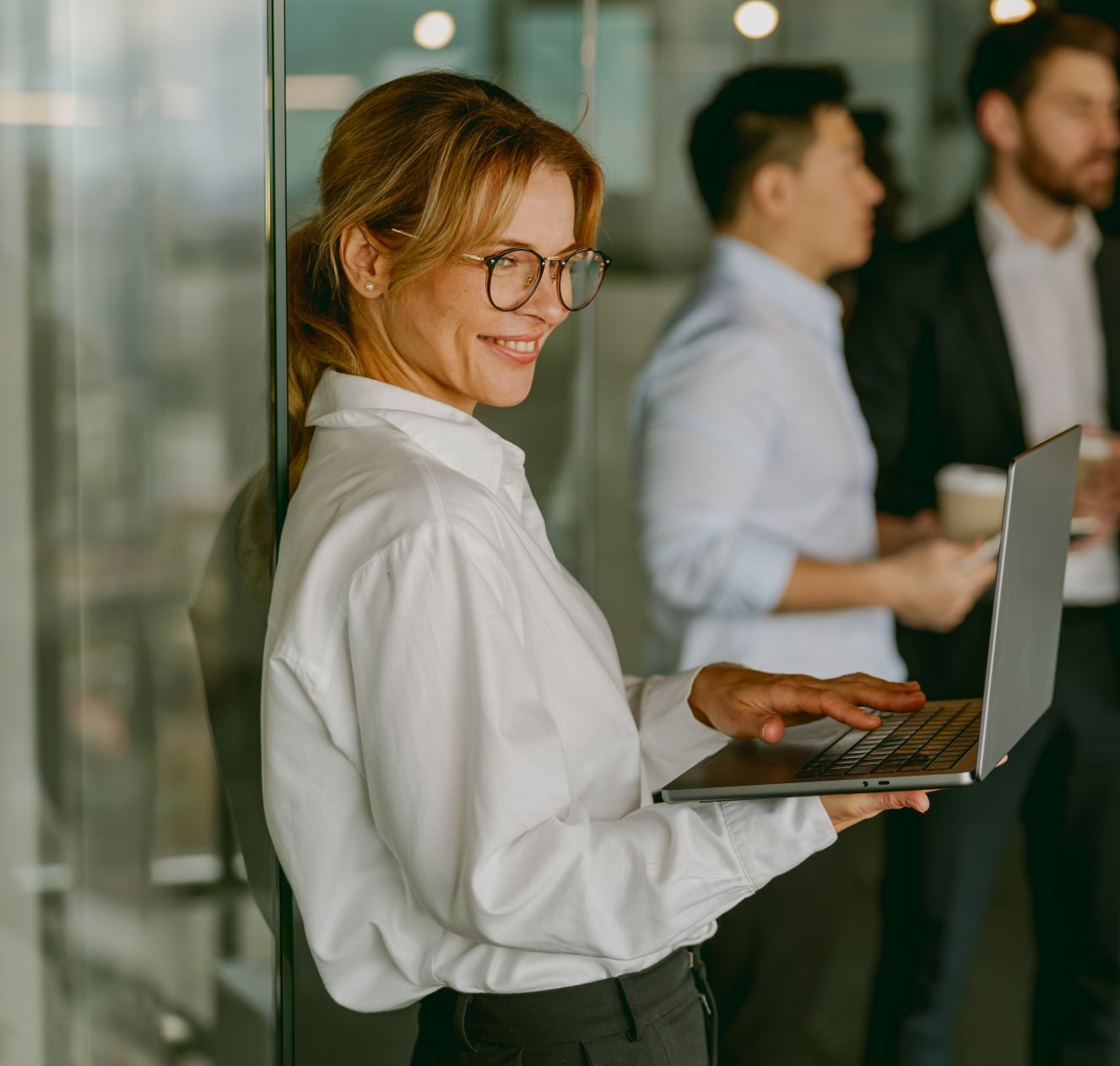 Businessfrau mit Laptop im Vordergrund, Team im Hintergrund bei der OM Analyse