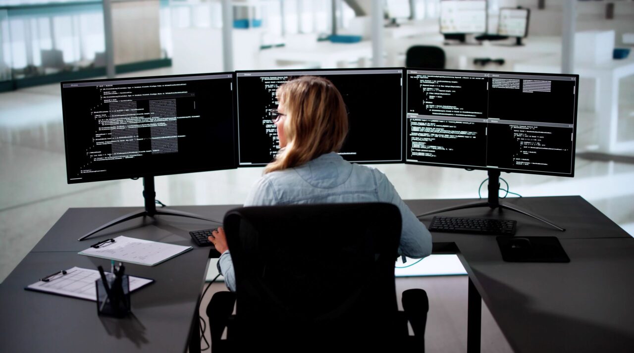 Eine Entwicklerin arbeitet in der Mendix-Plattform an mehreren Anwendungen gleichzeitig auf drei Monitoren. Enterprise & Solution Architecture für Unternehmen - Inacta