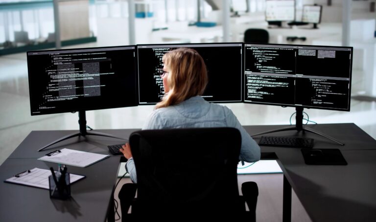 Eine Entwicklerin arbeitet in der Mendix-Plattform an mehreren Anwendungen gleichzeitig auf drei Monitoren. Enterprise & Solution Architecture für Unternehmen - Inacta